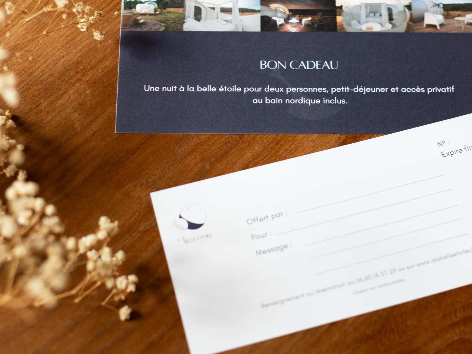 Les deux volets du bon cadeau imprimé, posés sur une table en bois à côté de fleurs séchées
