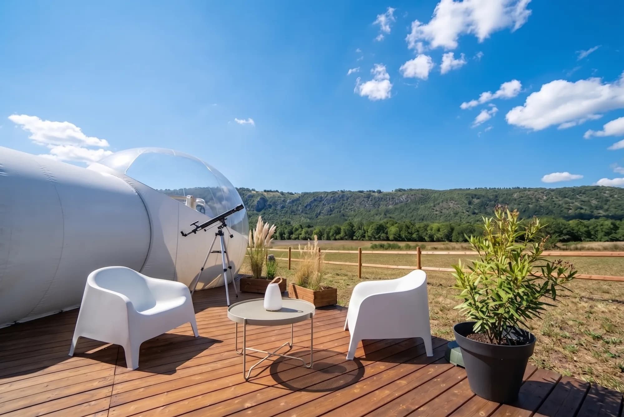 La bulle et sa terrasse en bois de jour, fauteuils et lunette d'astronomie devant les collines de la Suisse Normande